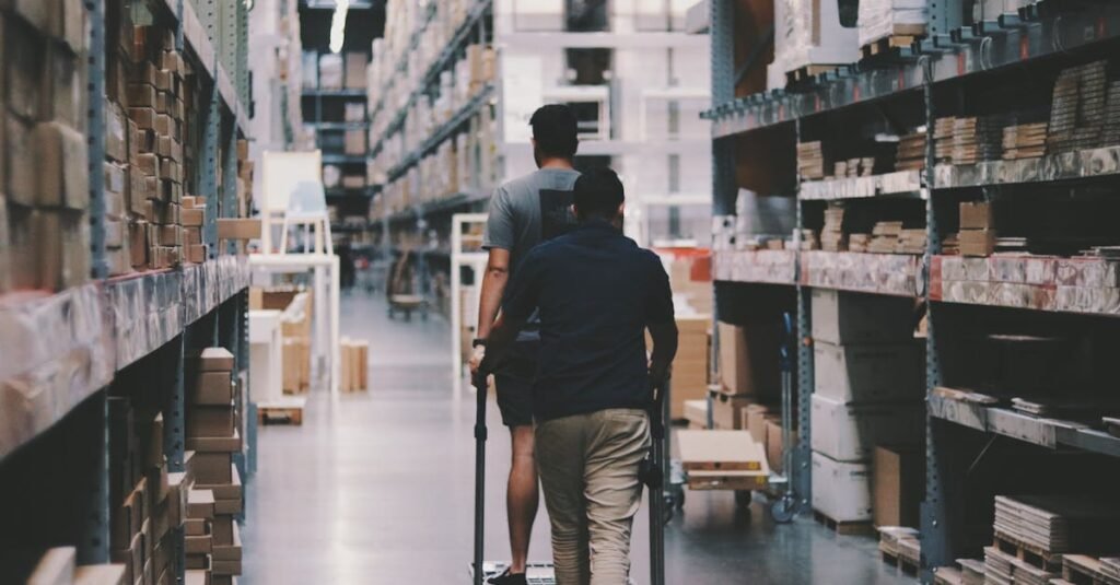 pexels-photo-1797428-1797428 Two men maneuver a trolley in a large warehouse filled with boxes and shelves.